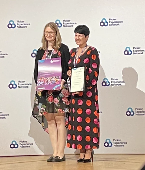 Picture shows 2 ladies standing in front of a picker experience Network Awards backdrop holding a runners up frame and poster