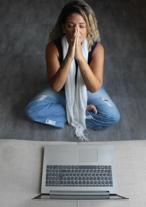 Photo of a woman praying in front of a laptop computer.