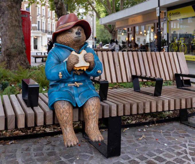 A statue of Paddington Bear sitting on a bench eating a marmalade sandwich
