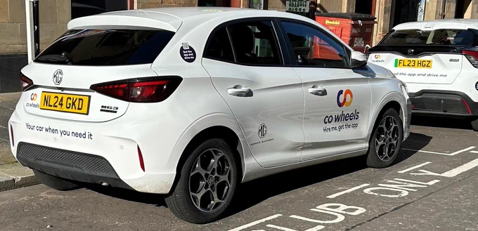 Car branded with Co Wheels car-sharing service logos parked in a designated spot on a city street.
