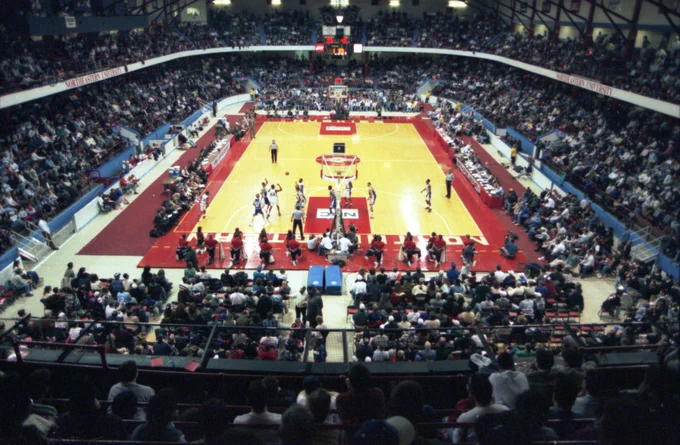 Panoramic view of a basketball court. A game is being played in front of a full crowd.