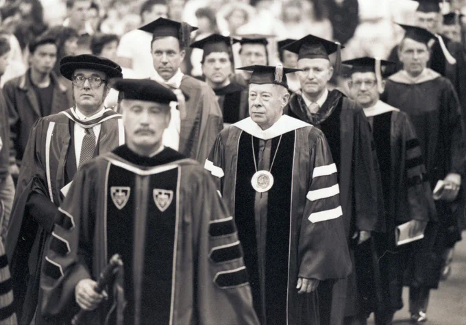 Black and white image of faculty members in graduation regalia walking in line