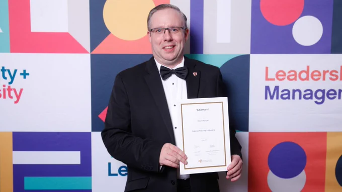 Dr Kevin Morgan, Queen's University Belfast, in formal dress holding his new National Teaching Fellowship award certificate at the awards ceremony, 2025.