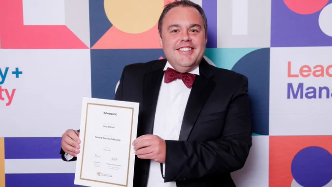 Dr Gary Mitchell MBE, Queen's University Belfast, in formal dress holding his new National Teaching Fellowship award certificate at the awards ceremony, 2025.