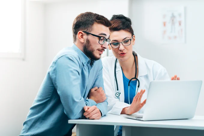 Two healthcare professionals in discussion over a laptop in a clinical office.