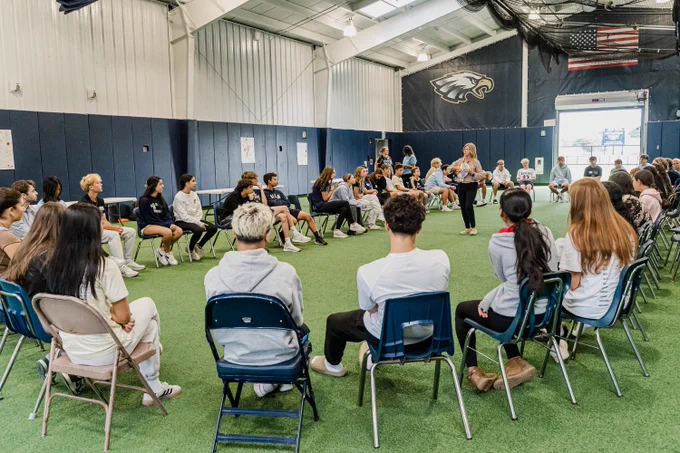 Students sit in a wide circle of chairs inside the athletic barn while an adult facilitator stands in the middle leading a Sources of Strength peer leader training activity.
