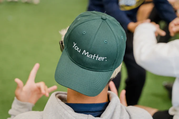 A student wearing a green baseball cap with the words “You Matter.” embroidered on the back, sits facing away from the camera.
