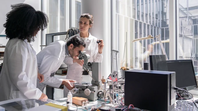 Researchers studying a microscope in the lab