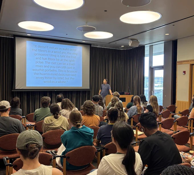 A seated audience faces a presenter and screen with a quote about writing.