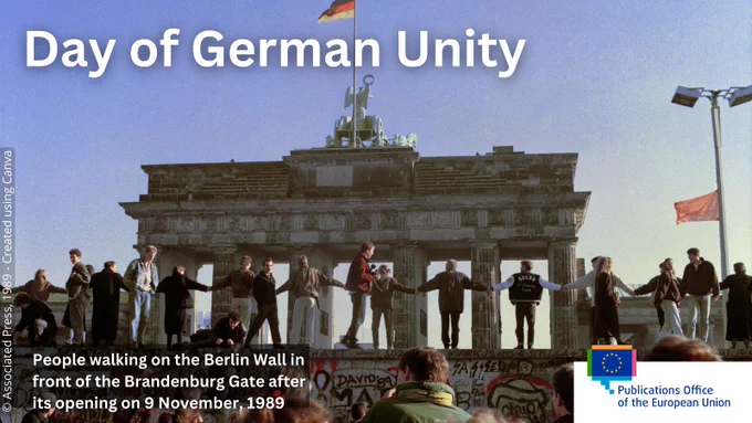 People singing and dancing on top of the Berlin Wall to celebrate the opening of East-West German borders following the fall of the wall on 9 November 1989. The large text says 'Day of German Unity'. 