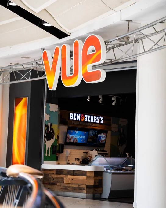 Entrance to a Vue cinema with a brightly lit orange and yellow logo above a Ben & Jerry's ice cream counter inside.
