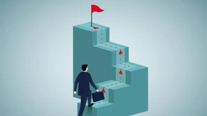 An illustration of a man in a business suit climbing a set of stairs toward a goal; a red flag is at the top of the stairs.