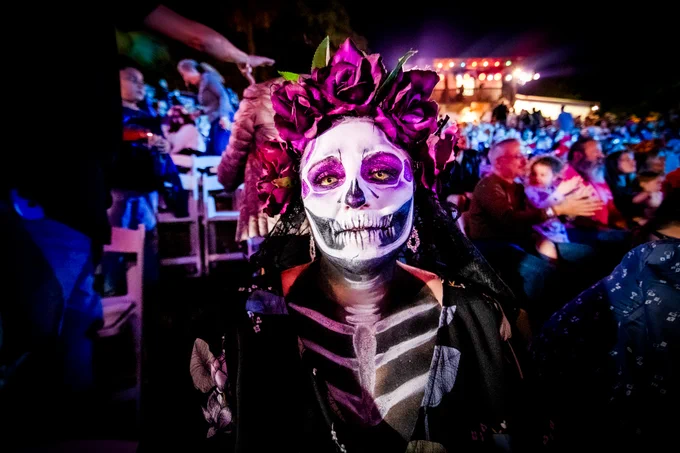 A person in a crowd wearing Día de los Muertos makeup and a hat of roses.