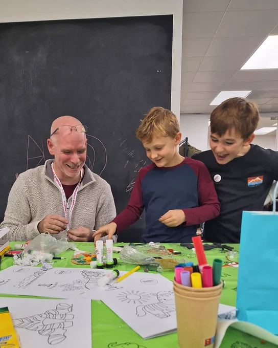 Man and two boys smiling while doing arts and crafts at a table.
