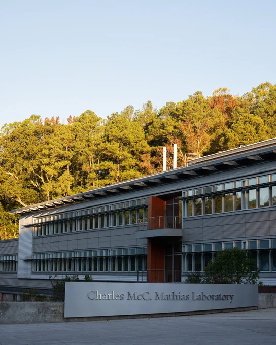 A two-story silver lab building with long rows of windows sits in front of a forest. A silver sign sits in front, with the words “Charles McC. Mathias Laboratory.”