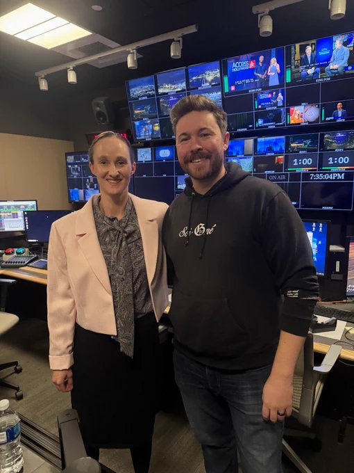 Katie Wilson stands in the control room of the television station studio with a supporter in a pink jacket.