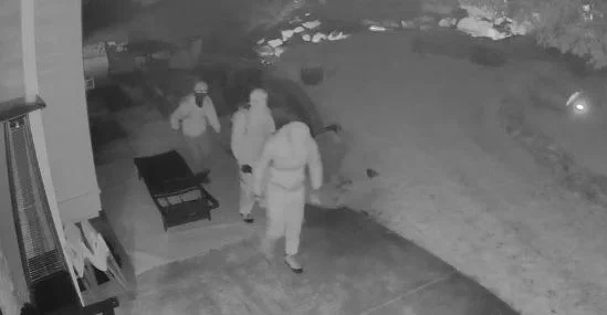 Surveillance photo showing three people in hoodies and masks walking 