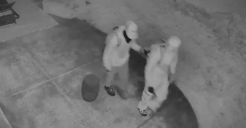 Surveillance photo showing two people in hoodies and masks walking 