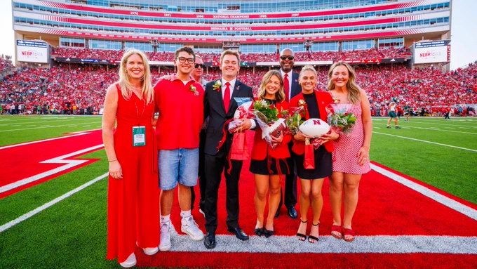 Four women and three men in red and black attire pose for a photograph at midfield in Memorial Stadium. (Kristen Labadie/University Communication and Marketing)