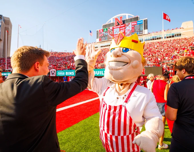 Homecoming royalty winner Caden Connelly high-fives mascot Herbie Husker, wearing red-and-white overalls and a gold crown, on the sideline at Memorial Stadium. (Kristen Labadie/University Communication and Marketing)