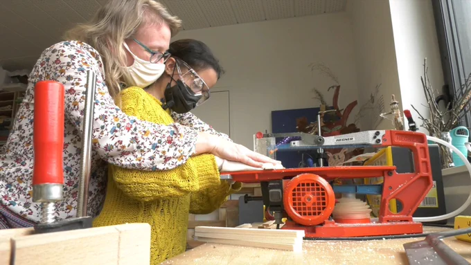 Une enseignante aide une élève avec du bois sur la scie à chantourner.