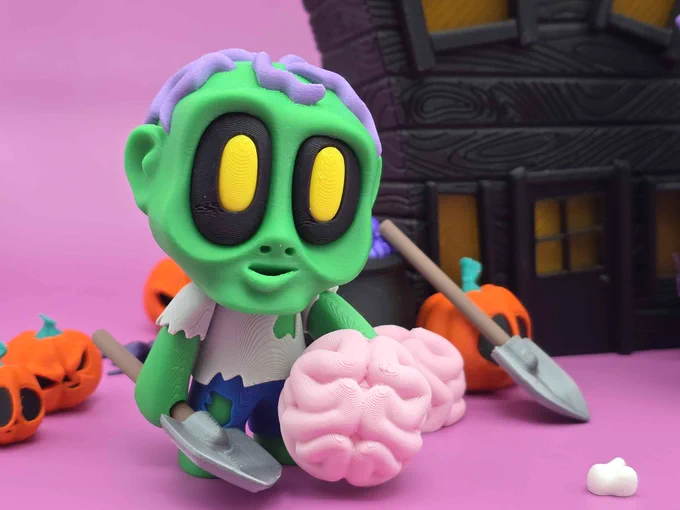 Close-up of the green 3D-printed Zombie Boy figure holding a pink brain and a gray shovel, surrounded by pumpkins and graveyard props.