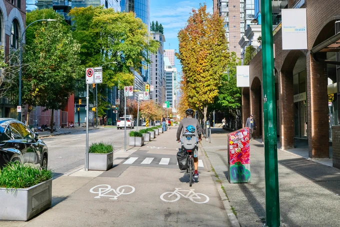 People of all ages and abilities ride bicycles on protected cycling infrastructure on the streets of Downtown Vancouver.