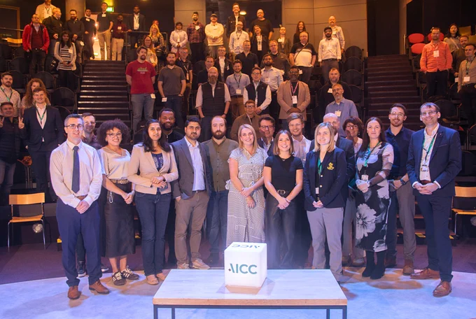 Large group of professionals posing in an auditorium with a cube labeled ICC on a table in front of them.