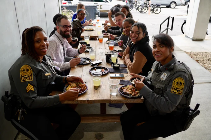 A table of V-C-U Police officers and staff members sitting at tables with plates of food, smiling.
