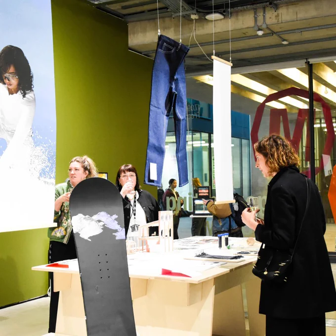 Visitors viewing an installation with hanging denim jeans and creative works displayed on tables.