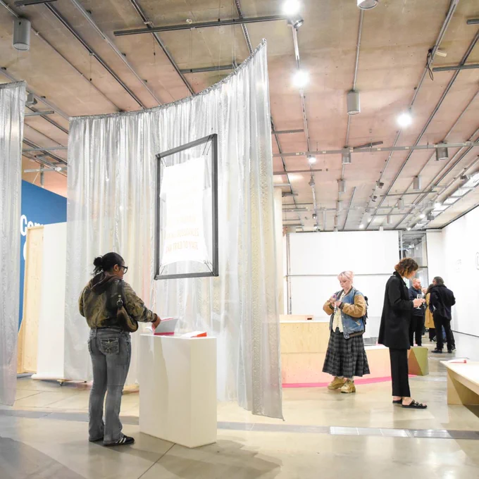Gallery visitors exploring artworks in a space with silver curtains and bright lighting.