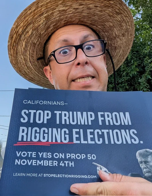 Ed Hernandez canvassing in San Leandro, wearing a straw hat and glasses, holding a Prop 50 sign to rally support for fair elections and voter empowerment in California.