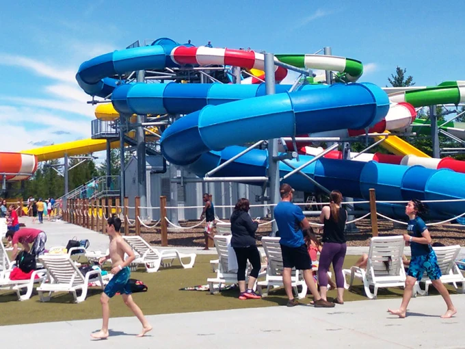 Photo: Visitors enjoying a sunny day at a waterpark with multiple colorful water slides and lounge chairs.