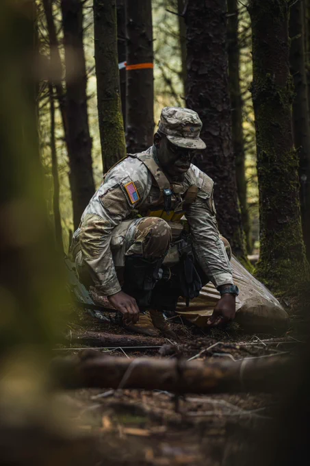 A soldier in camouflage uniform crouches while making a model of the ground.
