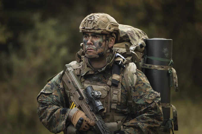A soldier wearing camouflage uniform carries his kit and his rifle on a patrol.