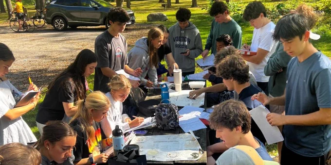 Group of students from Victor Senior High School engaged in an outdoor activity, working at a table with papers and water bottles in a park setting.