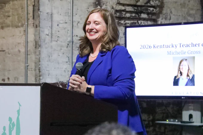 Michelle Gross smiles while holding a microphone and standing behind a podium
