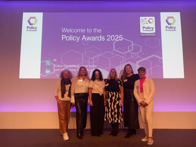 Photo of six women, including Assistant Director Emer Loughran, standing smiling in front of a large powerpoint slide 
