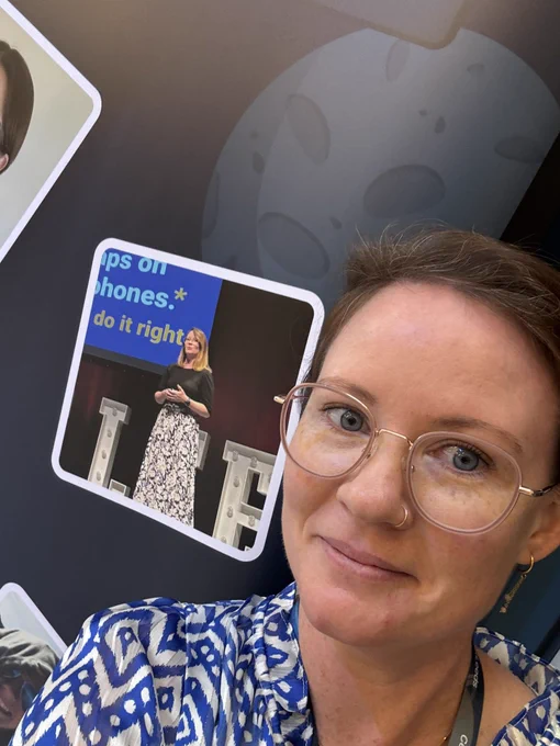 A selfie of myself with a poster with a picture of myself right behind me. I am half smiling awkwardly because there is a picture of myself on the wall