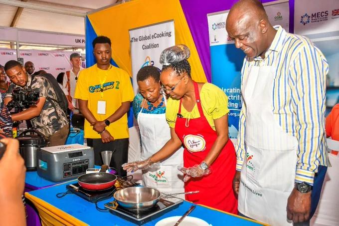 An exhibition area with a few African ladies and gentlemen gathering around a table where a female chef is demonstrating how to cook using an induction stove. 