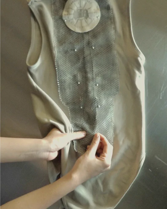 Hands adjusting a beige top with mesh fabric and small beads.