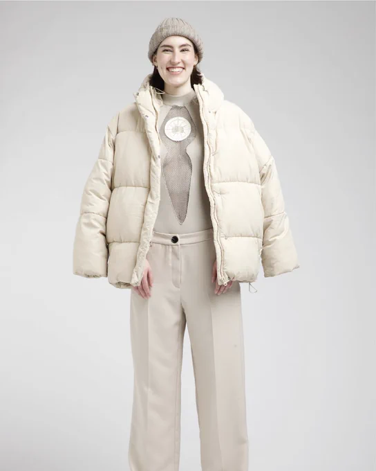 Model smiling, wearing a beige puffer jacket, knit beanie and sleeveless top with mesh cut-out.