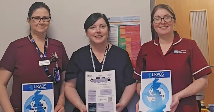 Three female nurses standing together, holding posters with information about Acute Oncology