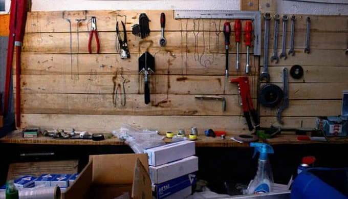 Organized garage workbench with hanging tools, screwdrivers, pliers, and wrenches neatly arranged on a wooden wall — part of a five-day garage decluttering project.