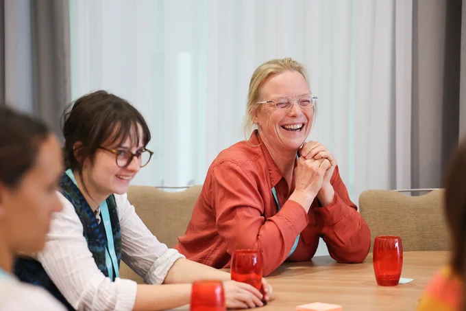 Group of people sitting around a table engaged in a discussion with red glasses on the table.