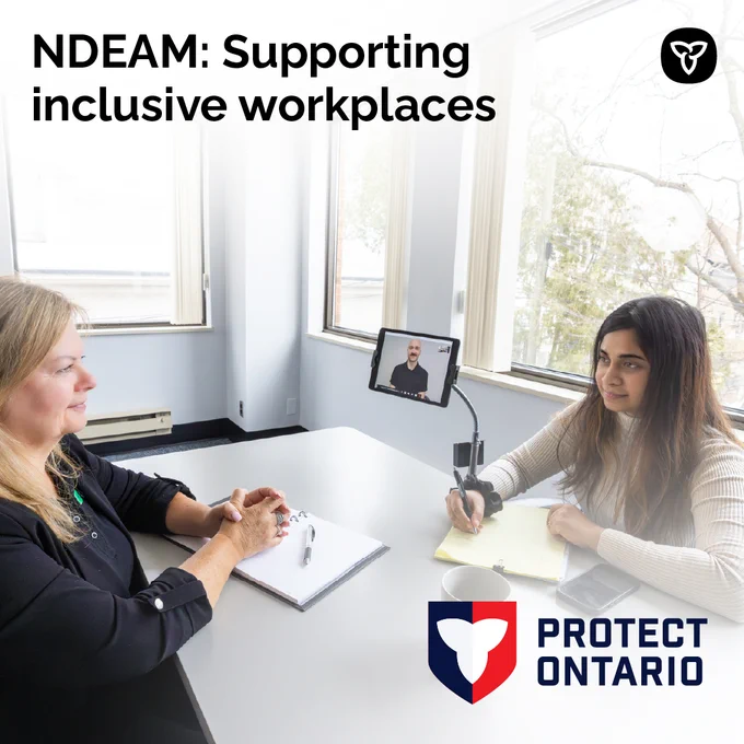 Two adults sitting at a table. One person takes notes while another person uses a portable ASL interpreting service through a device. Text reads: NDEAM: Supporting inclusive workplaces. 