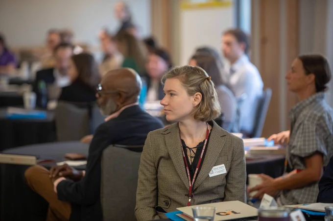 people seated at tables listening to a speaker at the front of the room at the ten across convergence meeting