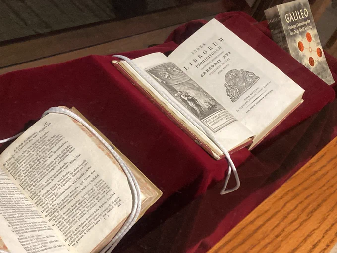 Photo of books on display in an exhibit case: 1744 and 1841 editions of the Index Librorum Prohibitorum (Index of Prohibited Books). A modern edition of Galileo's Dialogue Concerning the Two Chief World Systems is also in the case.