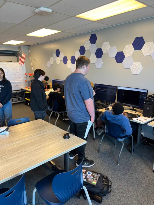 High school students working on computers with other students looking over their shoulders.