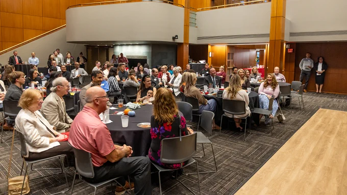 room full of people seated at round tables smile and laugh while listening to an award winner's remarks at the EDAD Impact and Inspiration Awards
